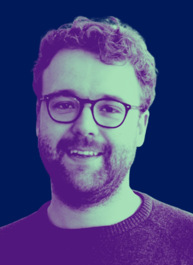 Duotone portrait of Ben Davies-Romano in purple and green against a deep blue background — smiling, with glasses, curly hair and a beard.
